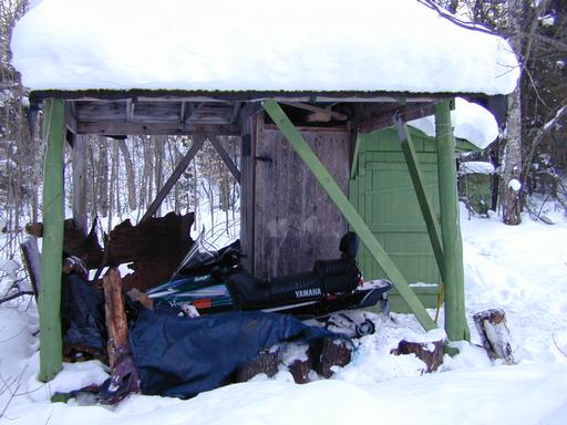 Snowmobile parked near the woodpile.
