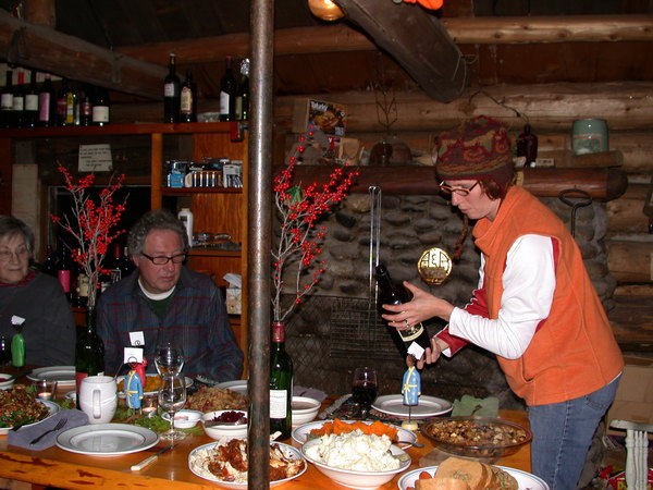 Thanksgiving dinner table with food.Amelia is pouring wine while Carl and Rose look on.